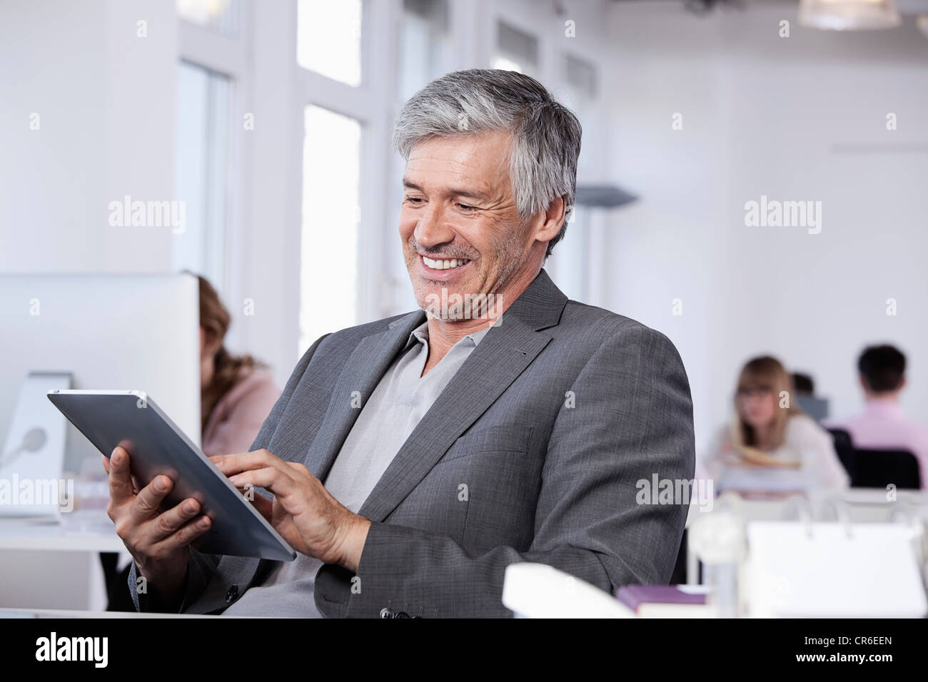 Deutschland, Bayern, München, reifer Mann mit digital-Tablette, im Hintergrund arbeitenden Kolleginnen und Kollegen Stockfoto