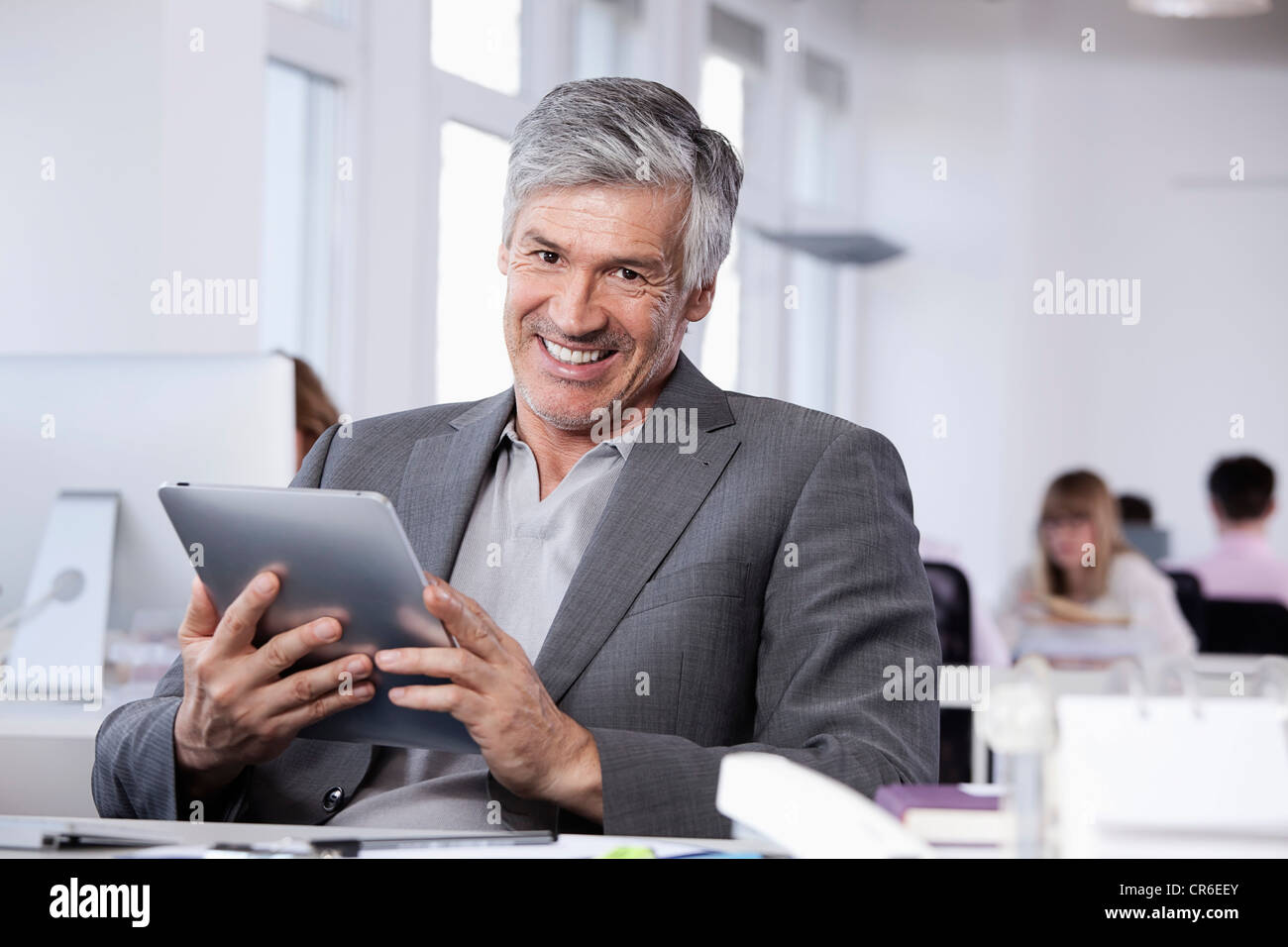 Deutschland, Bayern, München, reifer Mann mit digital-Tablette, im Hintergrund arbeitenden Kolleginnen und Kollegen Stockfoto