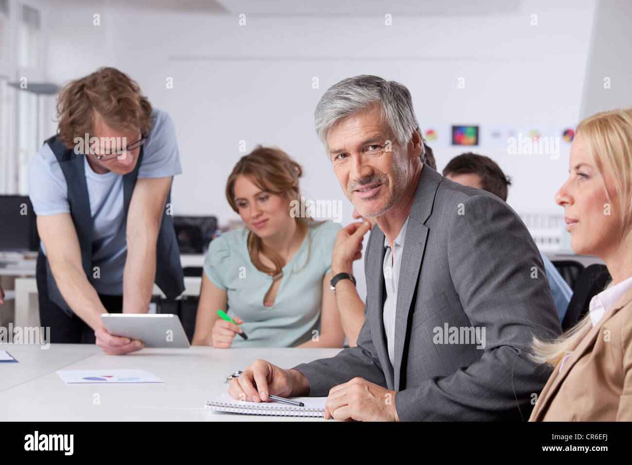 Deutschland, Bayern, München, reifer Mann lächelnd, während im Hintergrund arbeitenden Kolleginnen und Kollegen Stockfoto