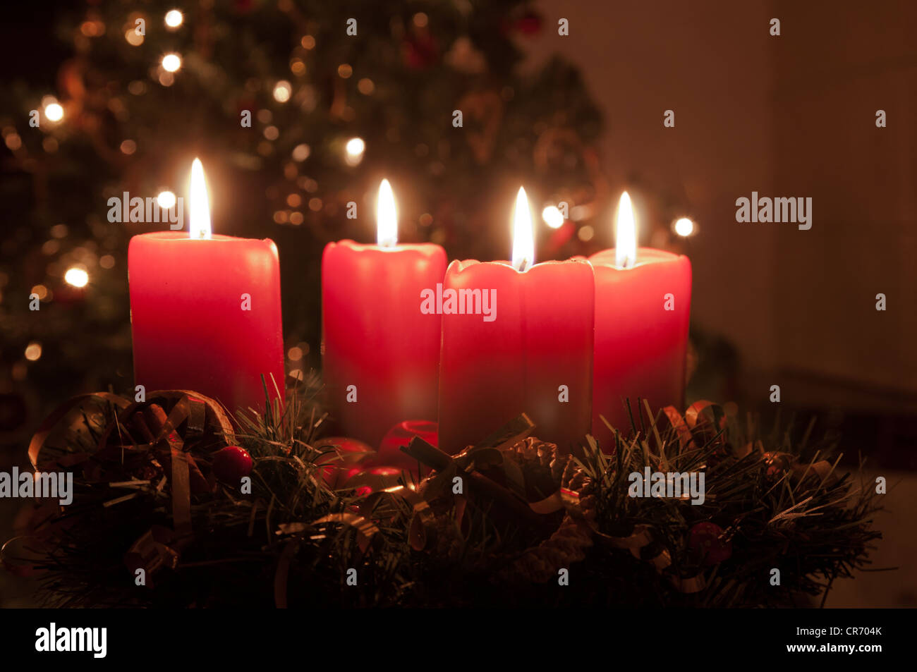 Weihnachten-Adventskranz mit roten brennenden Kerzen. Lichter auf x-mas Baum im Hintergrund Stockfoto