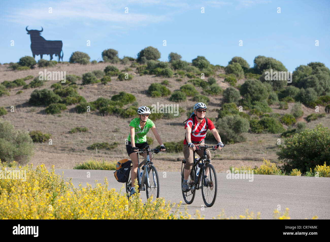 Spanien, Andalusien, Mann und Frau Reiten Fahrrad mit Stier-Statue im Hintergrund Stockfoto