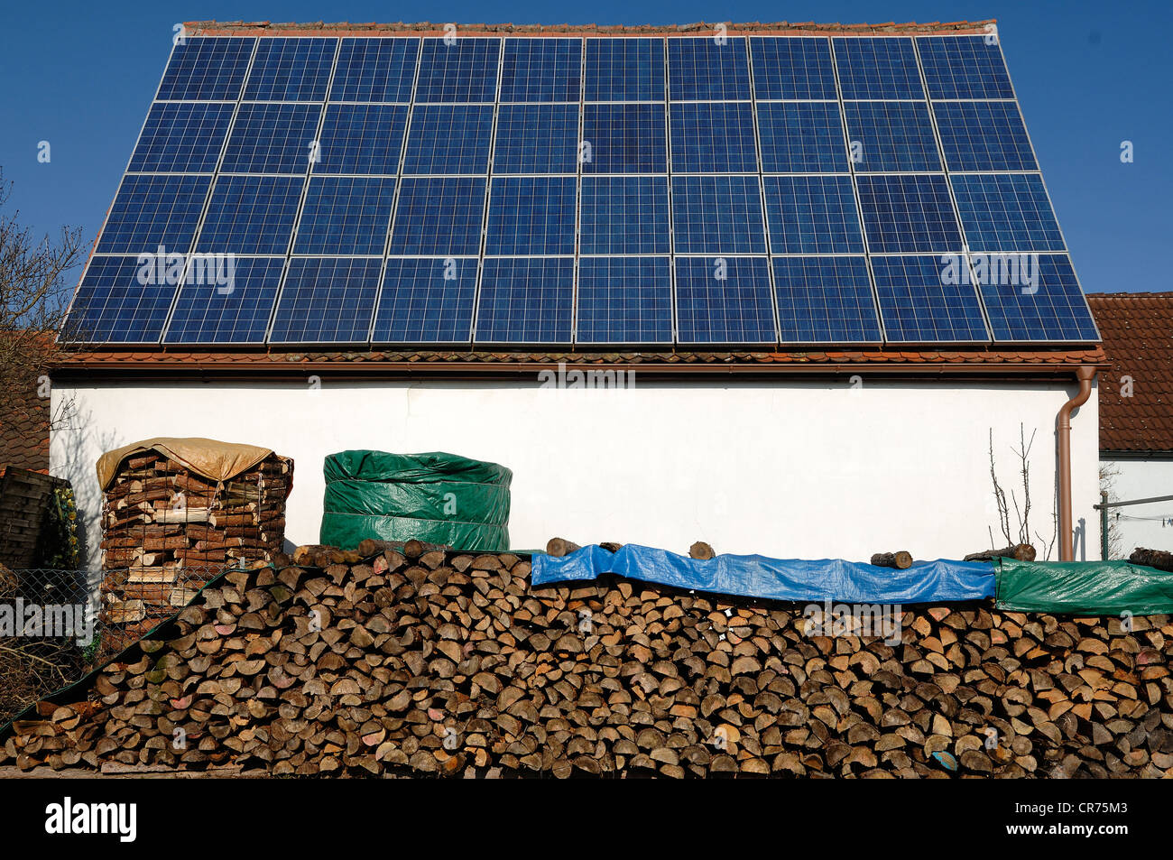 Photovoltaik-Anlage auf den Geräteschuppen eines Bauernhofes mit Brennholz gestapelt in der Front, Kalchreuth, Middle Franconia, Bayern Stockfoto
