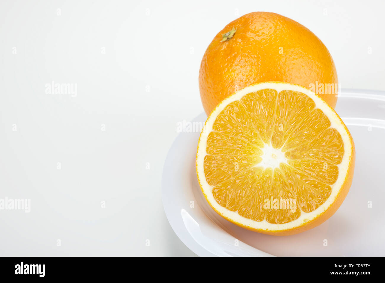 Zwei Orangen (Citrus Sinensis), eine ganze Frucht und einer halbierten Frucht, auf einem weißen Teller Stockfoto