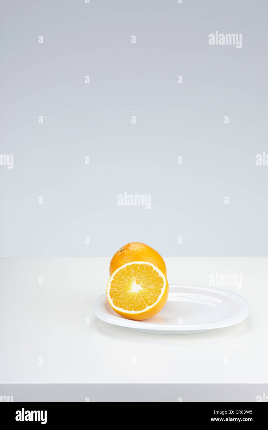 Zwei Orangen (Citrus Sinensis), eine ganze Frucht und einer halbierten Frucht, auf einem weißen Teller Stockfoto