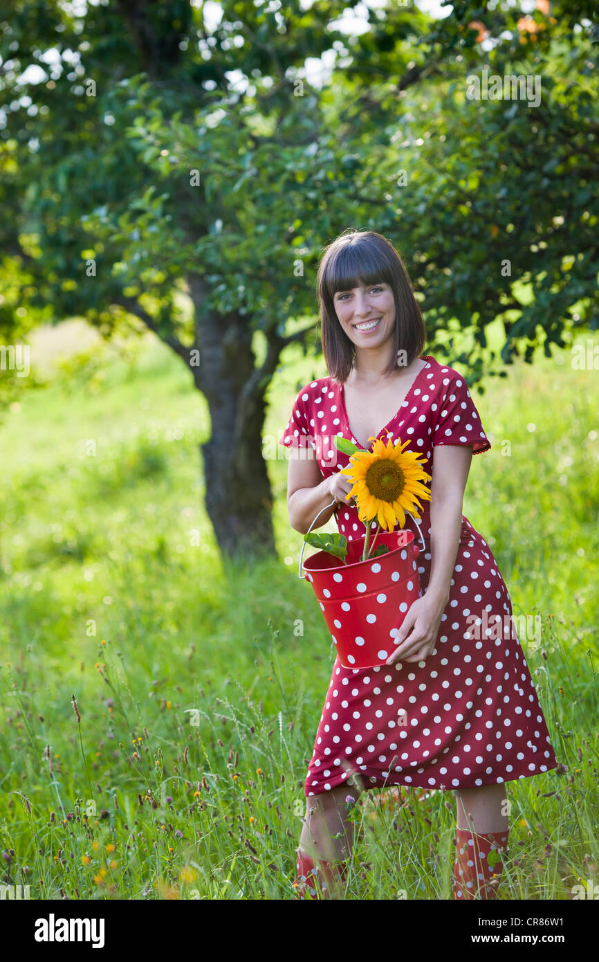 Junge Frau, 25, eine gefleckte Kleid trägt und hält eine Sonnenblume auf einer Wiese Stockfoto