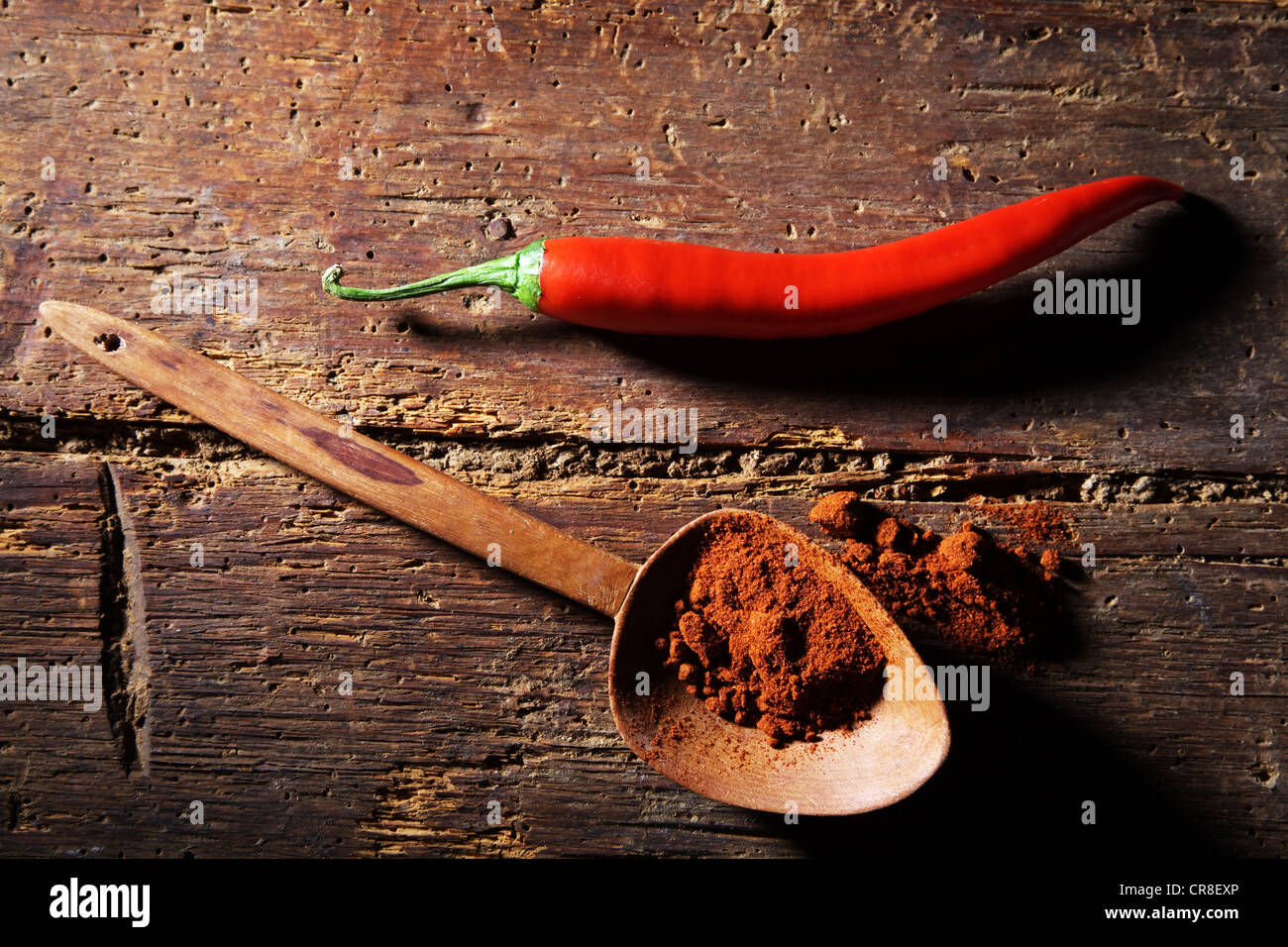 Chili-Pfeffer (Capsicum) mit einem Holzlöffel und Chilipulver auf einer rustikalen Holzoberfläche Stockfoto