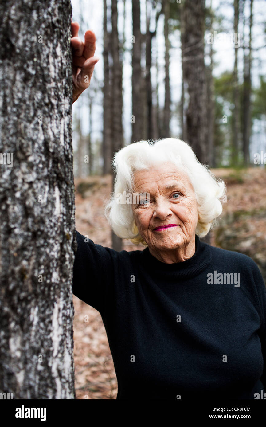 Porträt von senior Frau stützte sich auf Baumstamm im Wald Stockfoto