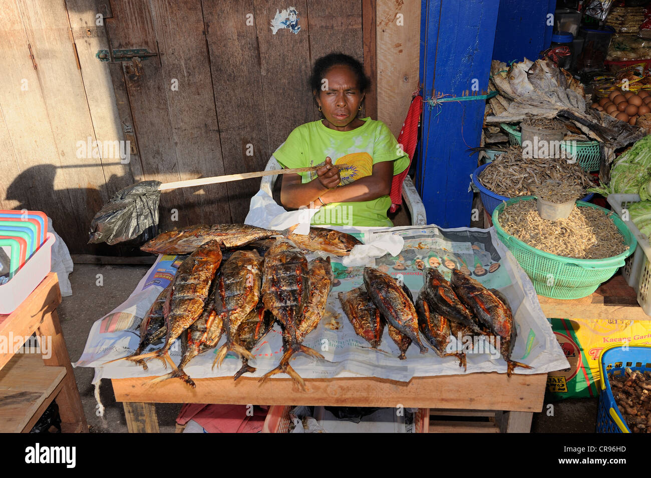 Papua-Frau gebratenen Fisch auf dem Fischmarkt in Kota Biak, winken die fliegen Weg mit einer Plastiktüte auf einem Stick zu verkaufen Stockfoto