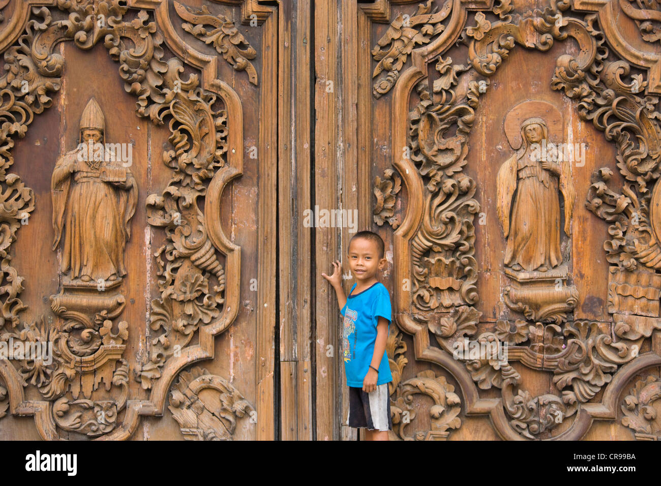 Boy von den kunstvoll geschnitzten hölzernen Tür am Eingang zur Kathedrale von Manila, Manila, Philippinen Stockfoto