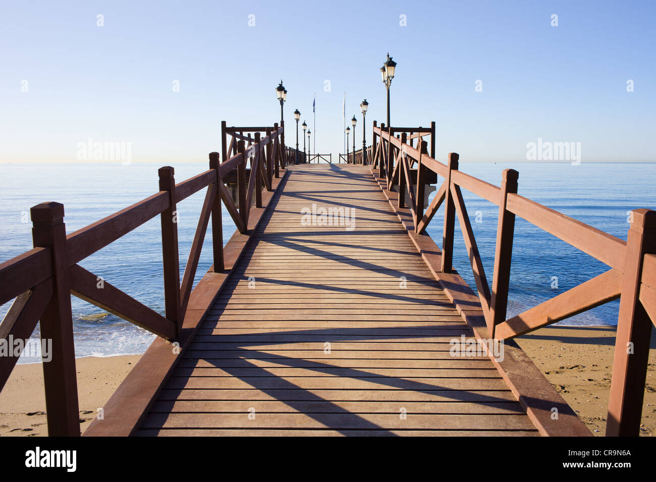 Holzmole in gutem Zustand mit Barrieren und Laternen auf einem ruhigen Mittelmeer in Marbella, Costa Del Sol, Spanien. Stockfoto