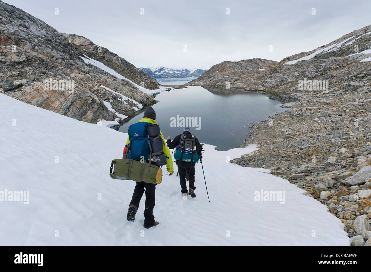 Wanderer mit Rucksäcken auf einem Feld von Schnee, See, am Sermilik Fjord, Ammassalik Halbinsel, Ostgrönland, Grönland Stockfoto