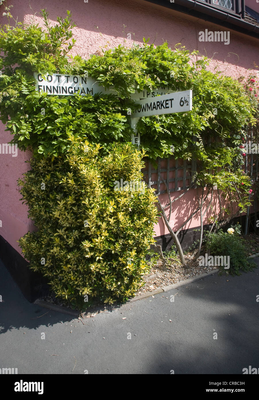 Dorf Richtung Straßenschild überwuchert an Hauswand Mendlesham, Suffolk, England Stockfoto