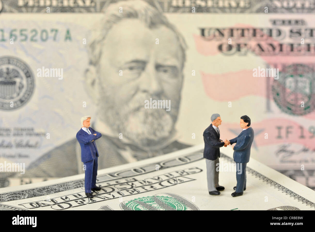 Miniatur-Figuren von Managern Händeschütteln beim stehen auf US-Dollar-Banknoten, symbolisches Bild für Unternehmen Stockfoto