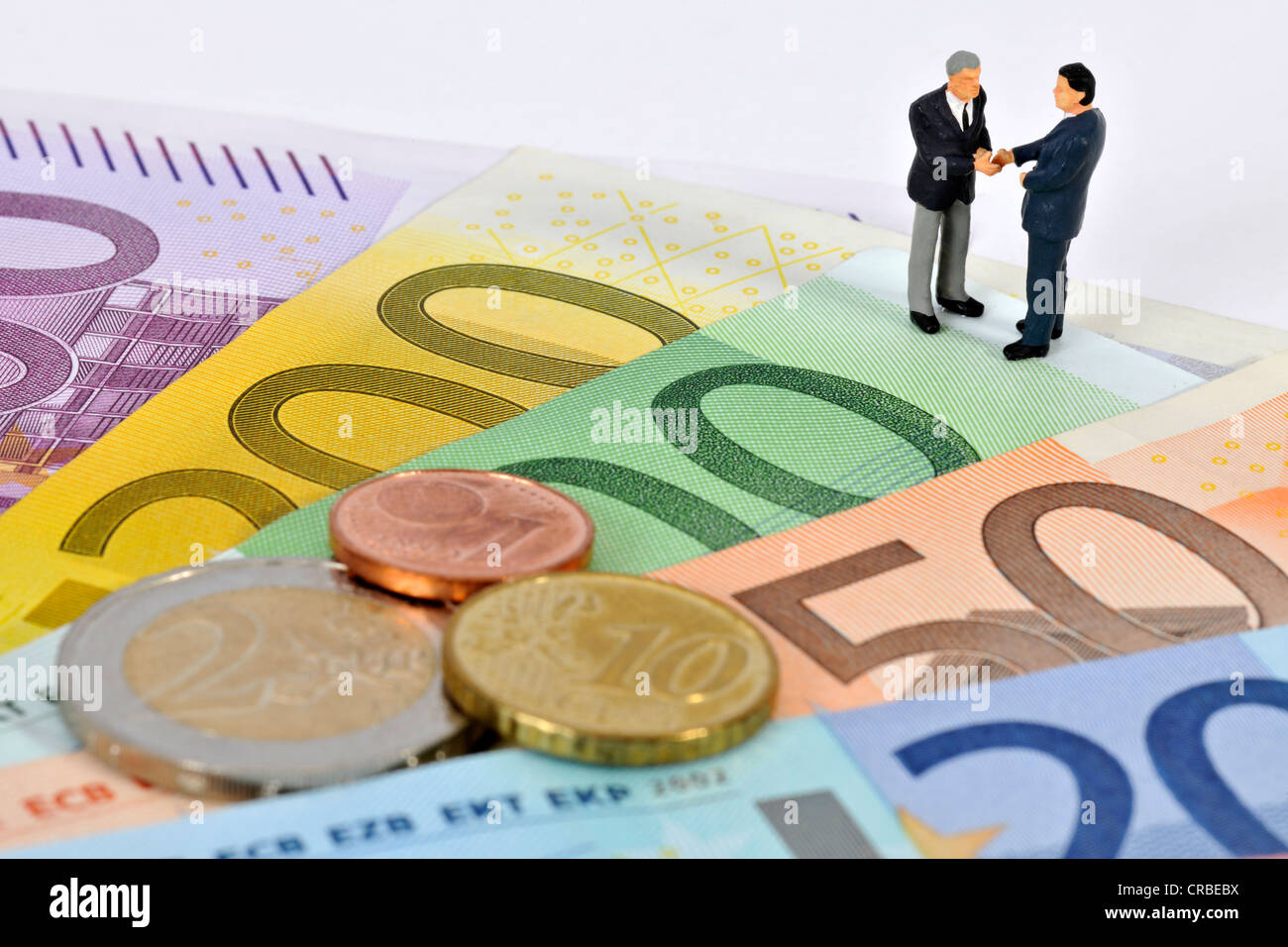 Miniatur-Figuren von Managern Händeschütteln beim stehen auf Euro-Banknoten und Münzen, symbolisches Bild für Unternehmen Stockfoto