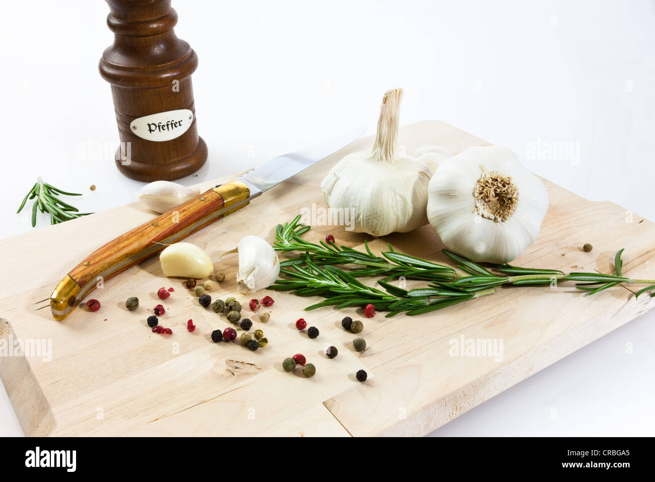 Knoblauch (Allium Sativum) auf einem Holzbrett mit Messer, Pfeffermühle, Rosmarin und schwarzem und rotem Pfeffer Stockfoto
