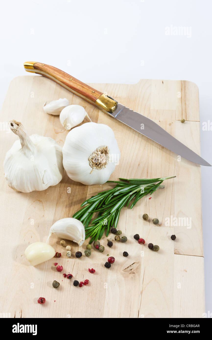 Knoblauch (Allium Sativum) auf einem Holzbrett mit Messer, Rosmarin und schwarzen und roten Pfeffer Stockfoto
