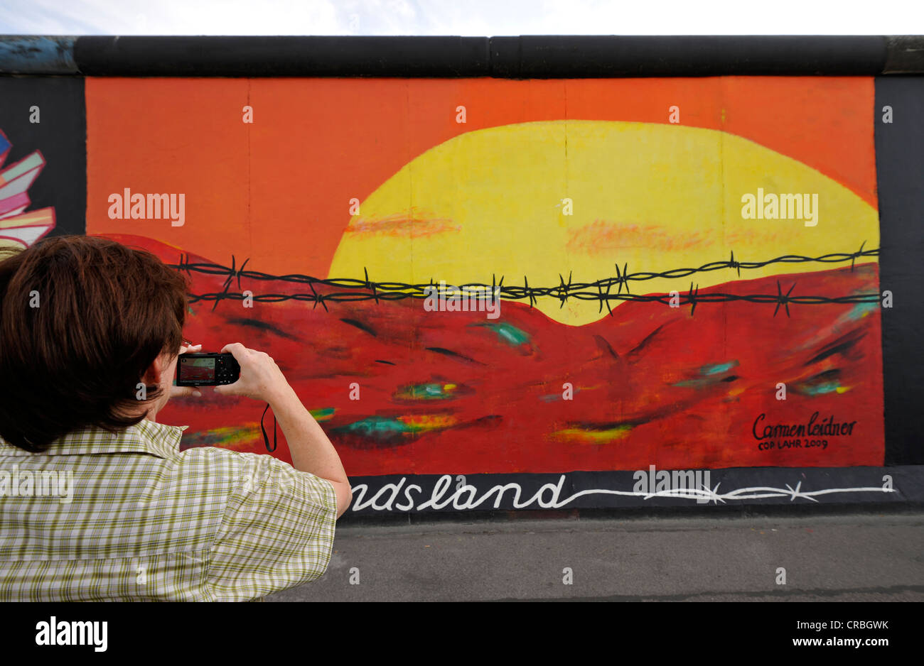 Touristen, die mit dem Fotografieren der Kunst und der Berliner Mauer, Sonnenaufgang im Osten hinter Stacheldraht, Malerei auf einem anderen Segment Stockfoto