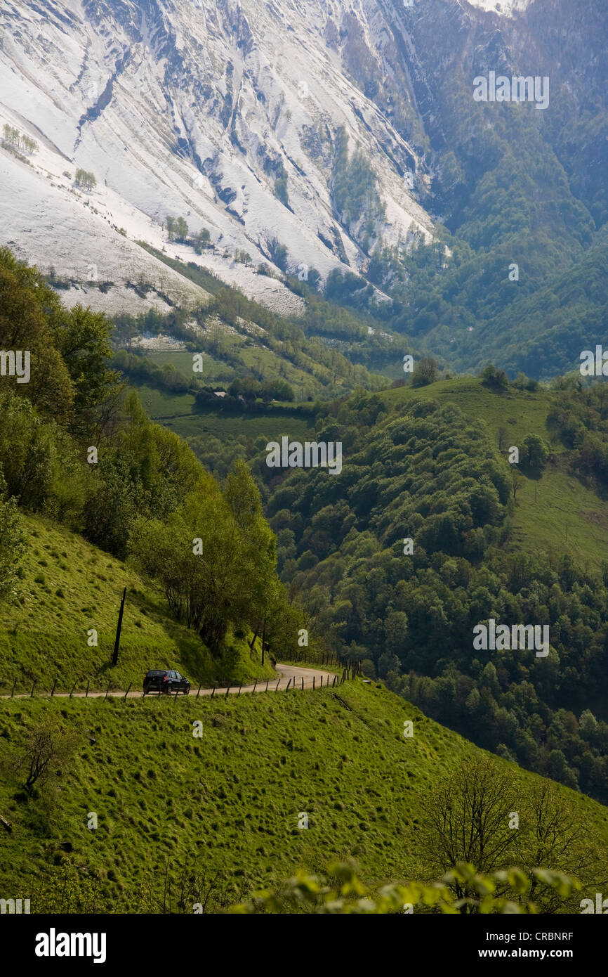 Eine Bergstraße windet sich von einem üppig grünen Tal auf schneebedeckten Berg in den französischen Pyrenäen. Stockfoto