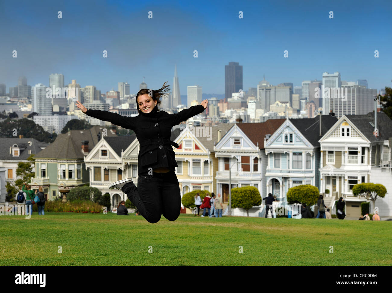 Junge weibliche Touristen springen in die Luft vor der Painted Ladies, Victorian, bunte Holzhäuser vor der Stockfoto