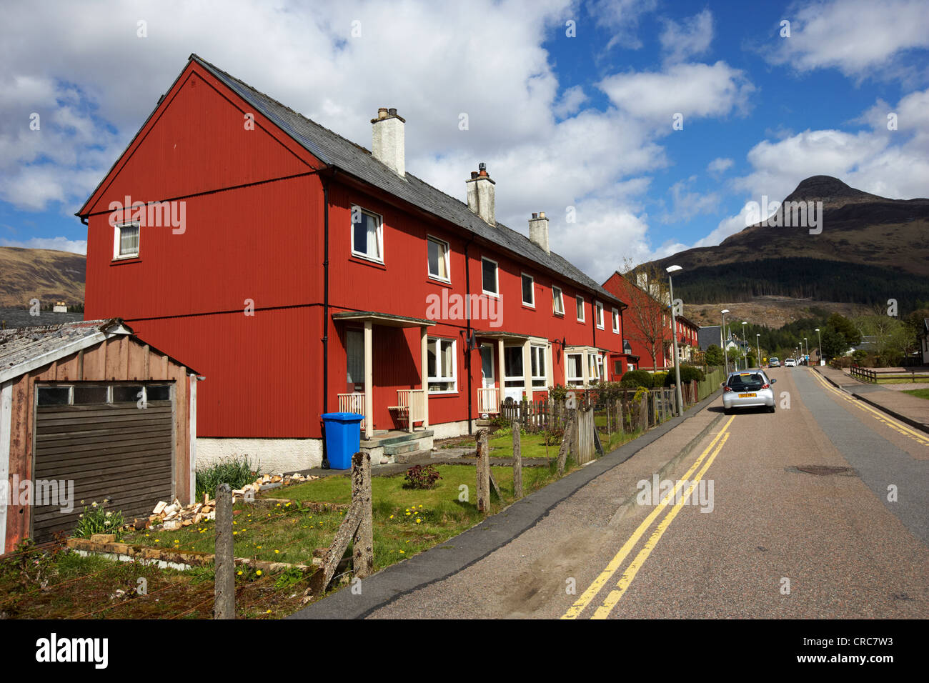 rot lackiert bekleideten Holzhäuser auf der Hauptstraße in Glencoe Hochland Schottland, Vereinigtes Königreich mit dem Pap von Glencoe im Hintergrund Stockfoto