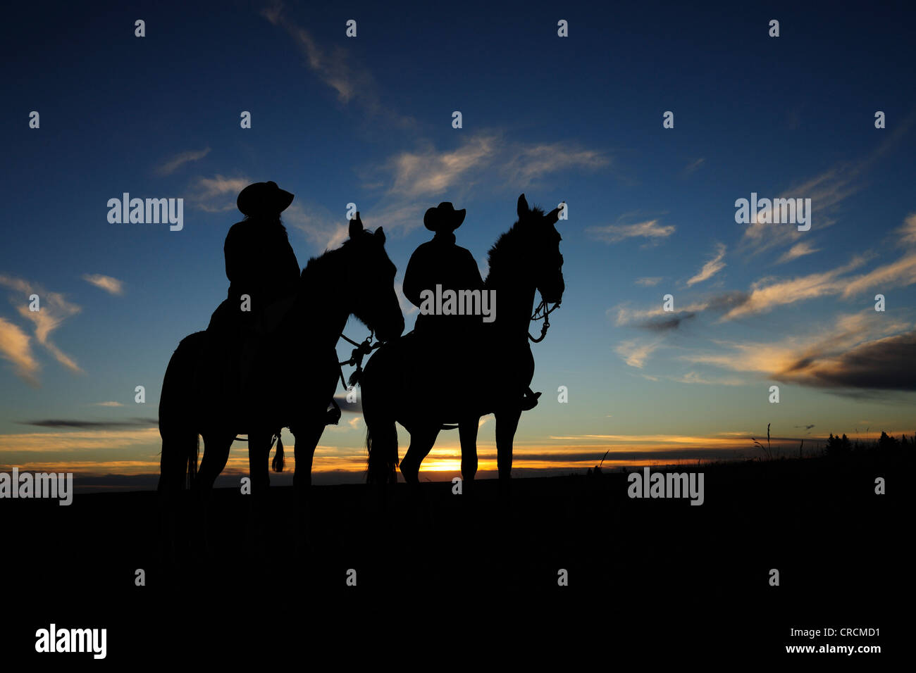 Ein Cowgirl und ein Cowboy sitzen auf ihren Pferden in den Sonnenuntergang, Saskatchewan, Kanada Stockfoto