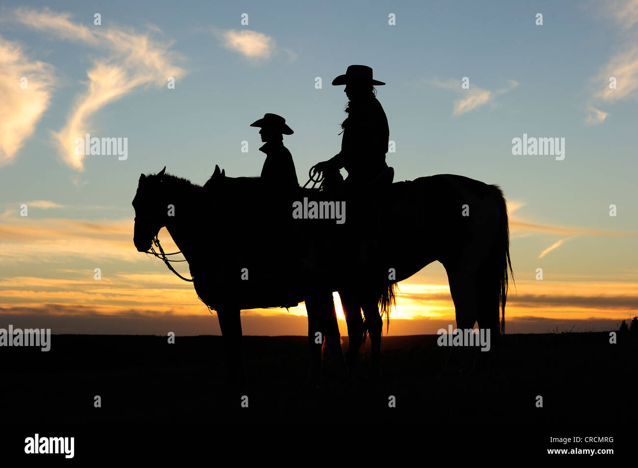 Cowgirl und Cowboy sitzt auf dem Pferderücken bei Sonnenuntergang, Saskatchewan, Kanada, Nordamerika Stockfoto