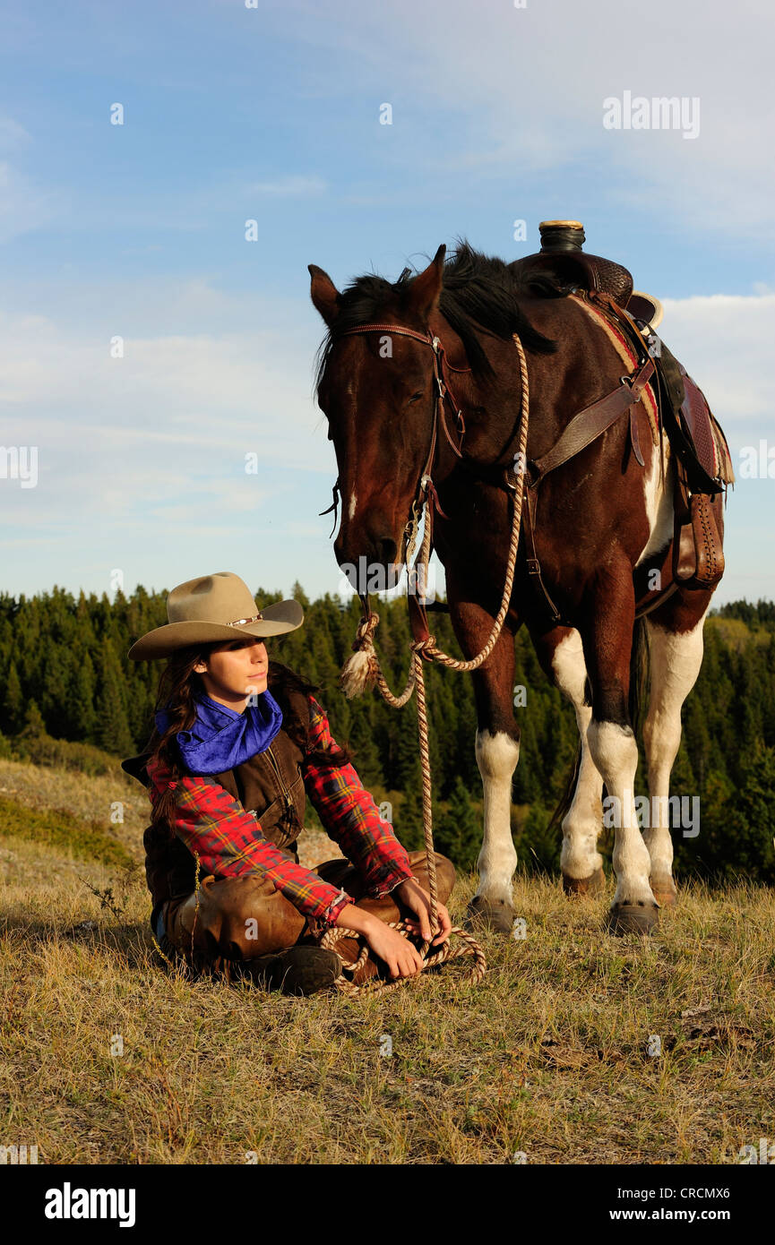 Cowgirl sitzt auf dem Boden neben einem Pferd, Saskatchewan, Kanada, Nordamerika Stockfoto
