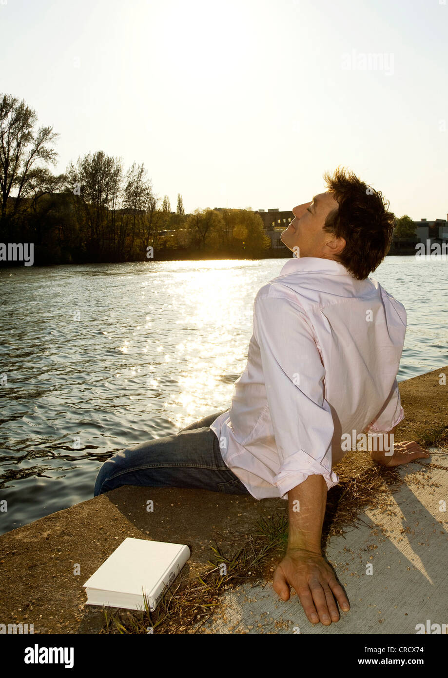 Mann sitzt am Flussufer Stockfoto