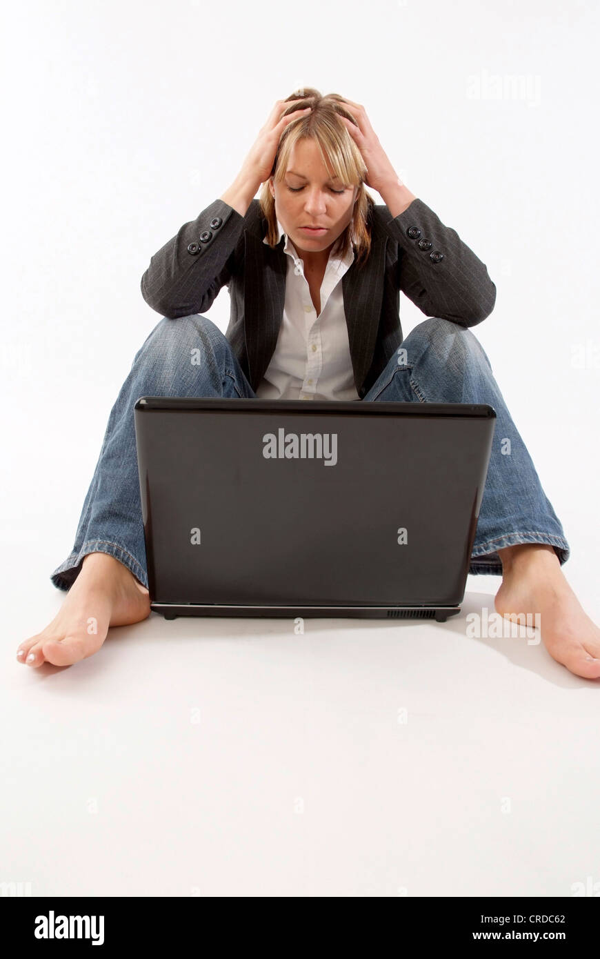 verzweifelte Frau sitzt vor ihrem Laptop, mit den Händen am Kopf Stockfoto
