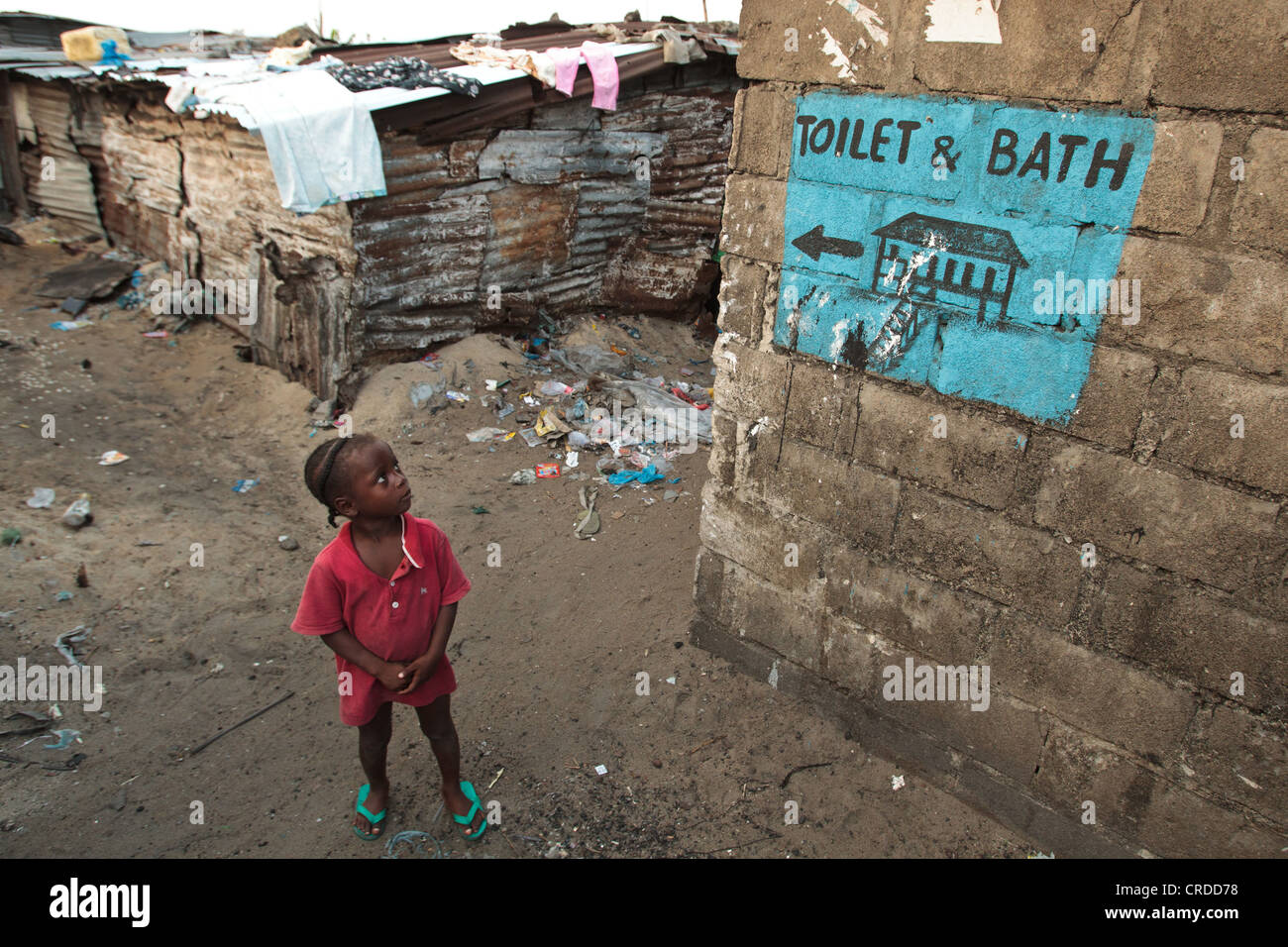 Eine Mädchen steht unter einem Gemälde, das angibt, Richtungen zu einem nahe gelegenen Toilette und Bad-Anlage in der West Point Slum in Monrovia Stockfoto