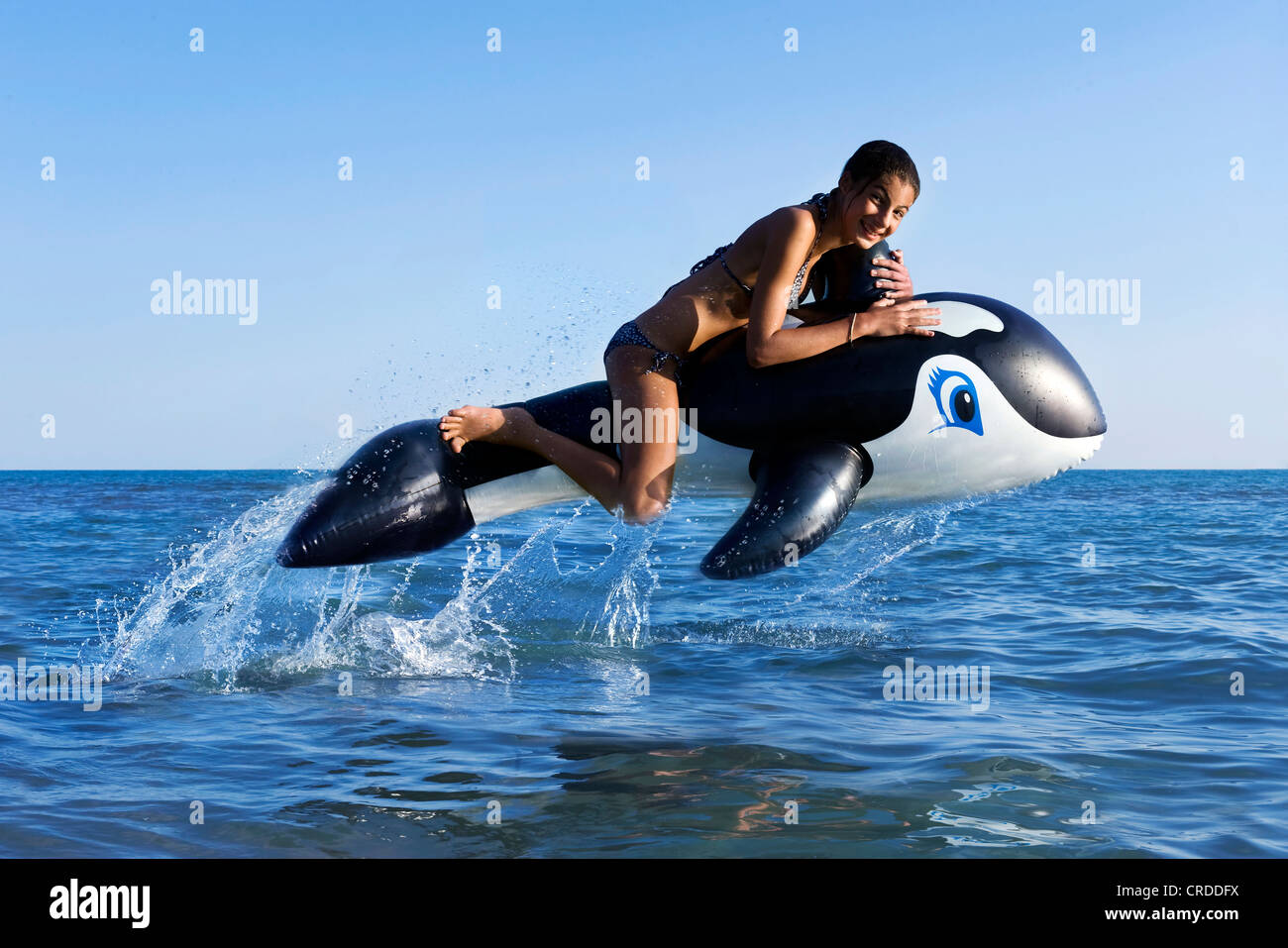 Mädchen sitzen auf aufblasbaren Orca im Meer springen Stockfoto