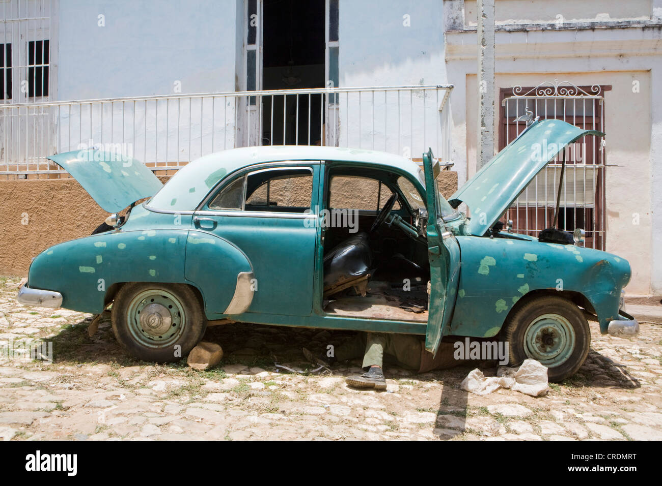 Mann liegt unter einem klassischen amerikanischen Auto in der Straße in der Altstadt von Trinidad, Kuba Stockfoto