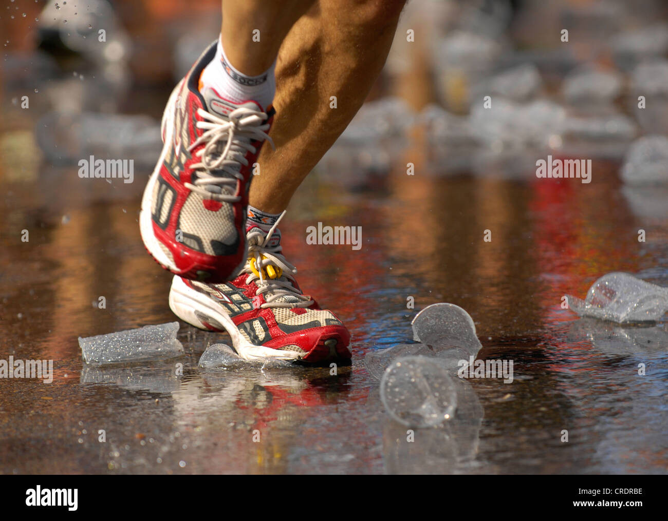 Marathon-Mann Schuhe eines Läufers auf nassen Straßen mit leeren Plastikbecher Stockfoto