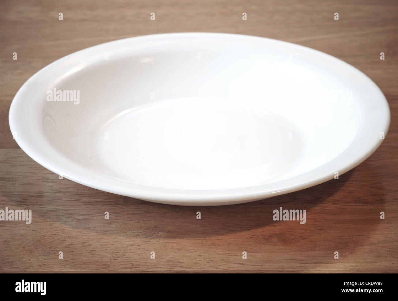 Leere weiße Platte im Winkel auf dem Holztisch Stockfoto