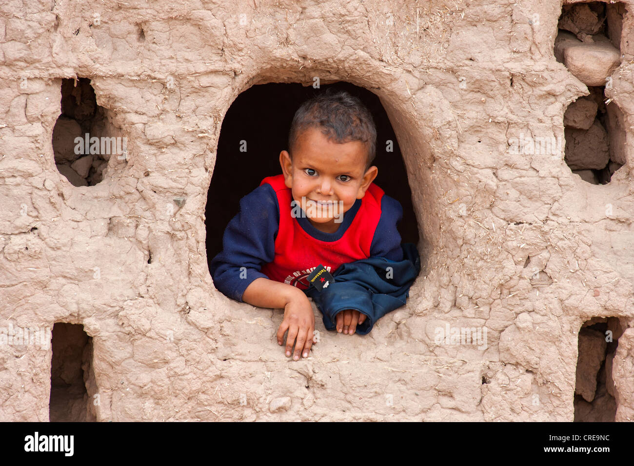 Ein kleiner Junge aus der Fensteröffnung eine abklingende Kasbah neugierig schauen, Tighremt oder Berber Wohnburg aus gemacht Stockfoto
