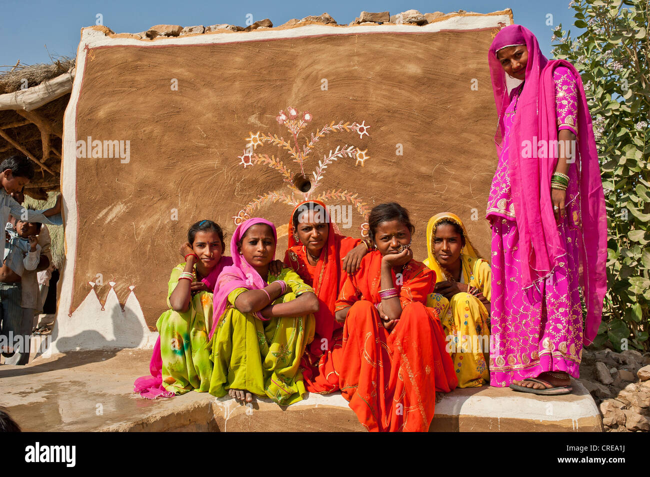 Junge Mädchen tragen leuchtend bunten Saris, einer Hochzeit, sitzen sie auf den Boden vor eine Wand bemalt mit Stockfoto