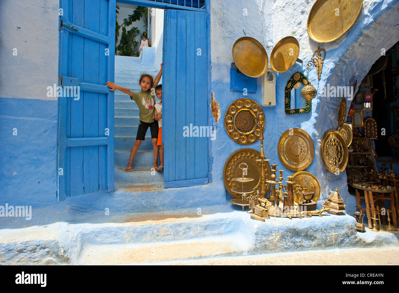 Zwei Kinder schauen neugierig aus einer Tür auf der rechten Seite die Ware der Kupfer und Messing Händler, Altstadt, Medina Stockfoto