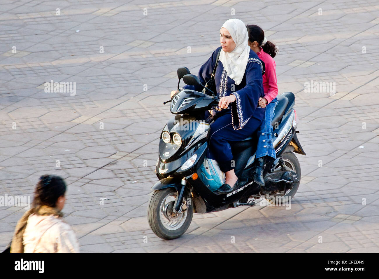 Frau auf einem Moped tragen traditionelle Djellaba in Djemaa El Fna Platz, Medina oder Altstadt, UNESCO-Weltkulturerbe Stockfoto