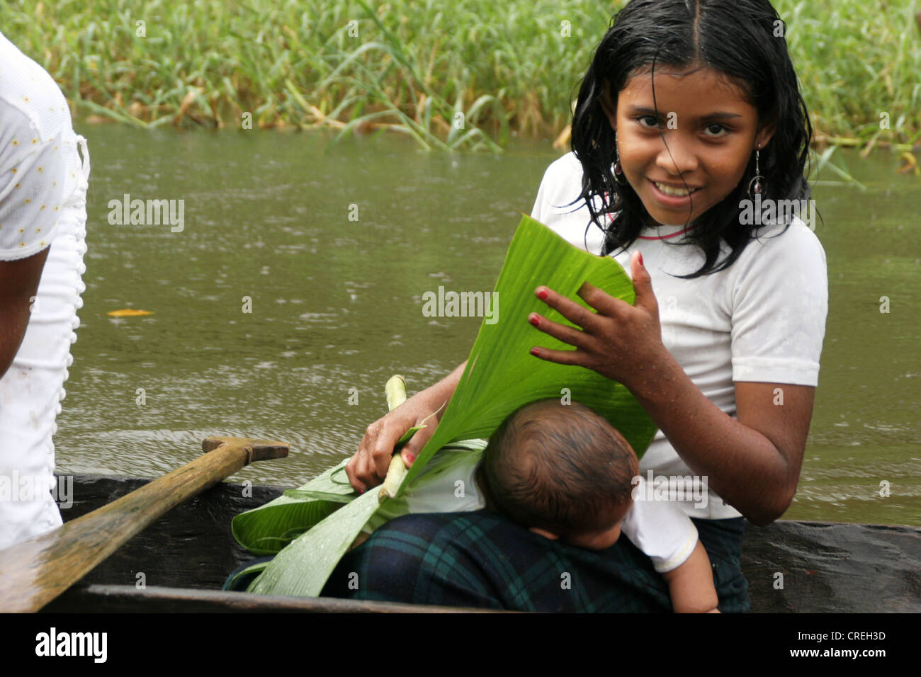 Kind in einen Unterstand, die versuchen, ein Baby mit einem Bananenblatt bei starkem Regen am Rio San Juan River, Nicaragua, Rio San Juan zu schützen Stockfoto
