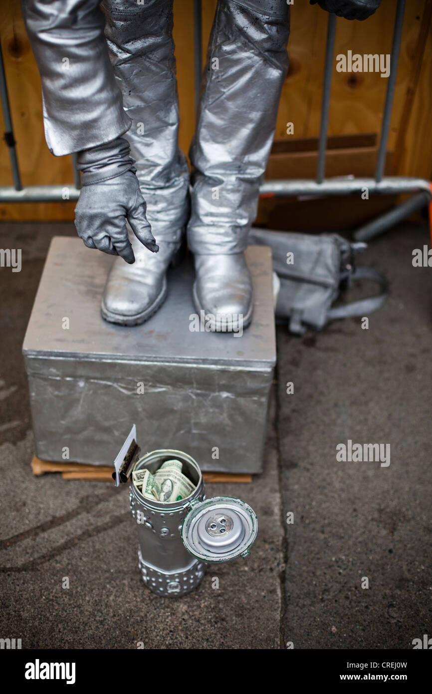A Street Performer in Silber gekleidet fällt einen Dollarschein in eine Dose. Stockfoto