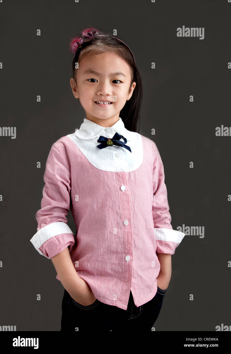 5 Jahre altes chinesisches Mädchen lächelnd, gekleidet in rosa Hemd und Jeans stehend mit Händen in den Taschen Stockfoto