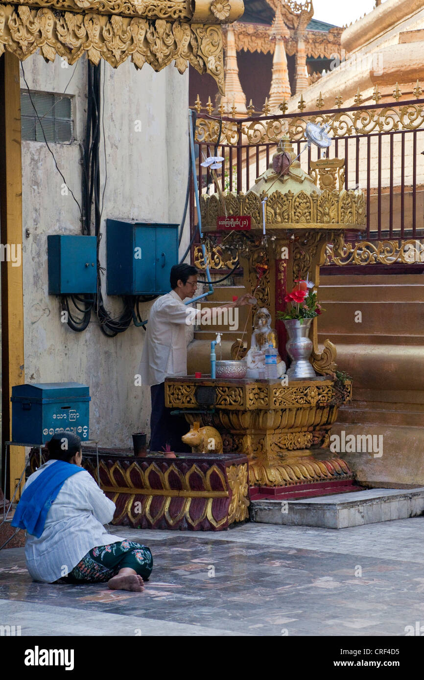 Myanmar, Burma, Yangon. Sule-Pagode. Frau beten während Man gießt Wasser über eine kleine Buddha-Statue. Stockfoto