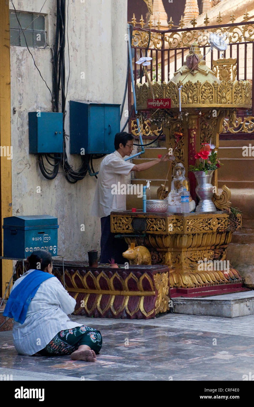 Myanmar, Burma, Yangon. Sule-Pagode. Frau beten während Man gießt Wasser über eine kleine Buddha-Statue. Stockfoto