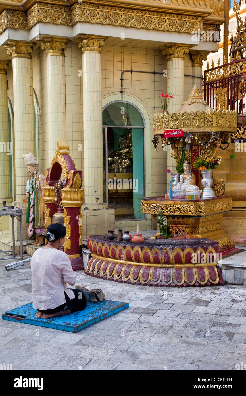 Myanmar, Burma, Yangon. Sule-Pagode. Frau beten vor Buddha-Statue. Stockfoto