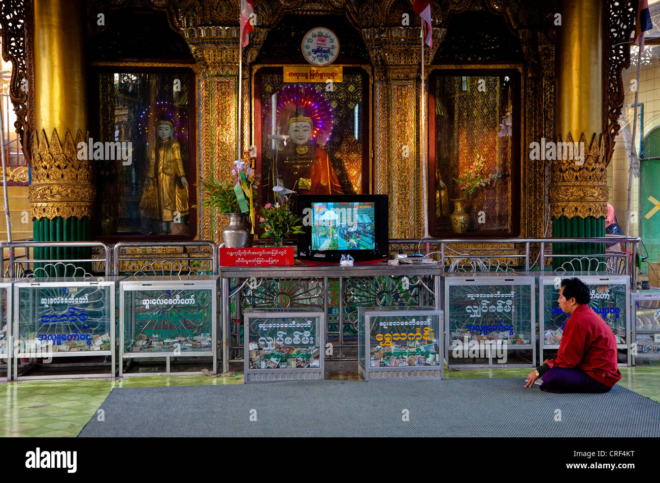 Myanmar, Burma, Yangon. Sule-Pagode. Menschen beten vor Buddha-Statuen, Fernseher. Stockfoto