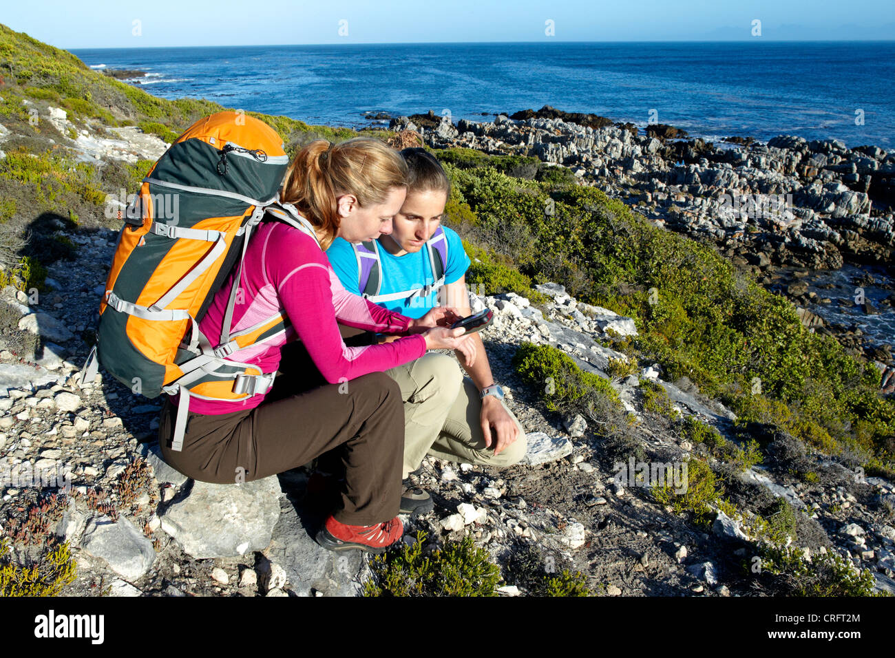 Zwei Frauen, ein GPS-Gerät beim Wandern auf einem Ozean Weg zwischen Gansbaai und De Kelders überprüfen. Südafrika. Stockfoto
