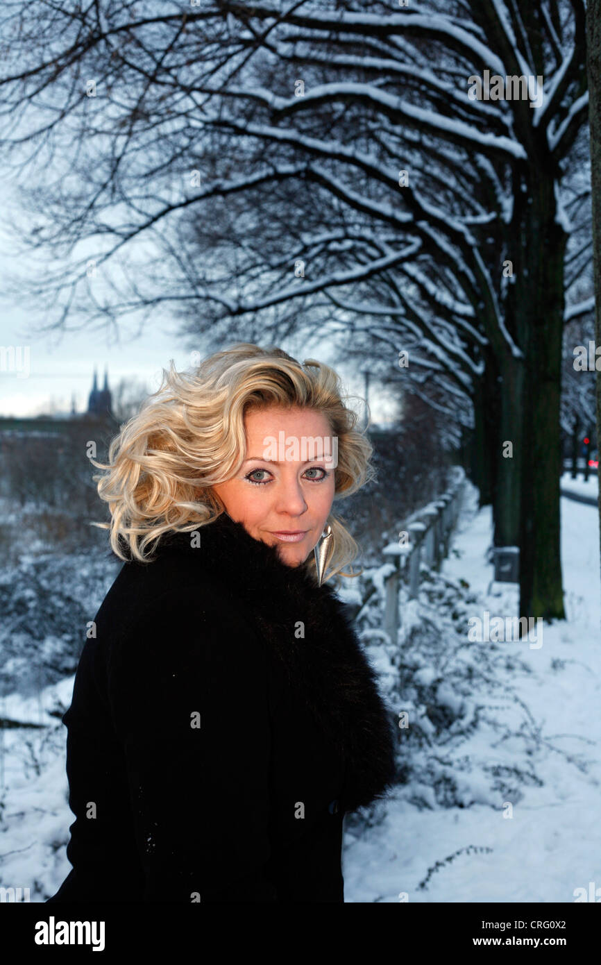 blonde Frau im schwarzen Mantel stehen im Schnee Stockfoto