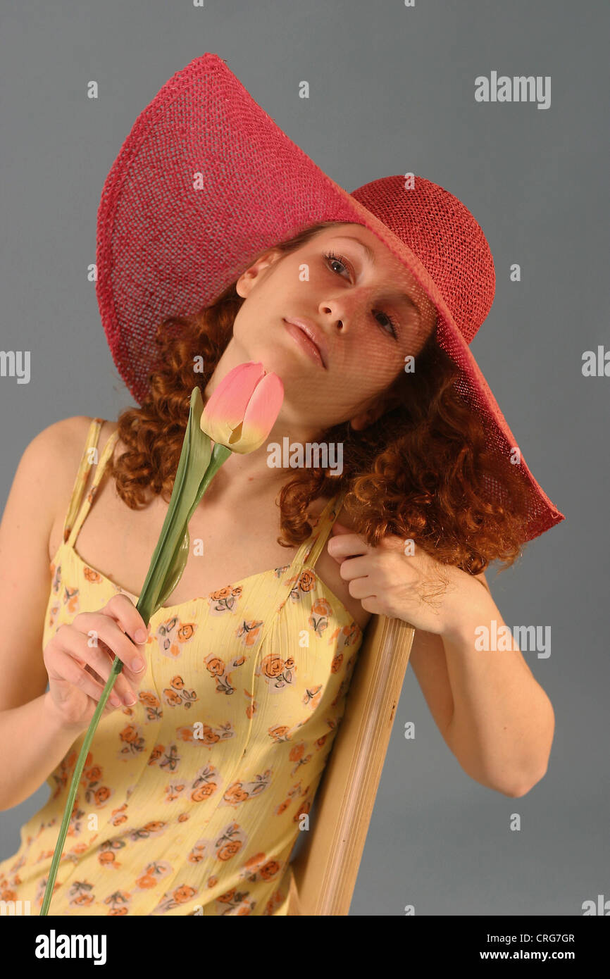 junge schöne rothaarige Frau mit großen roten Hut, riecht um eine Tulpe Stockfoto