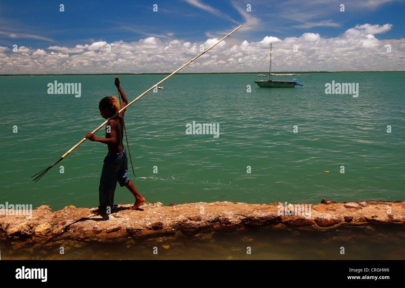 Junge mit Fisch Speer Spaziergänge unwirksam Ufermauer, Lage Insel, Torres-Strait, Australien. Papua Neu Guinea am Horizont Stockfoto