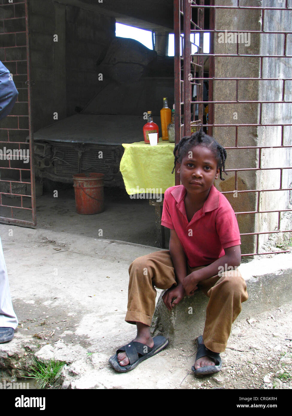 Kleiner Junge sitzt vor Garage er in dem lokal verkauft produzierte Alkohol nach niedergeschossen, Haiti, Provinz de l ' Ouest, Kenskoff, Port-Au-Prince Stockfoto